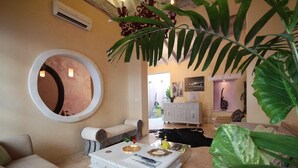 A living room with a round mirror, a white coffee table, and a sofa. There is a large plant in the foreground. - Casa Logos Comfort Stay (Cartagena)