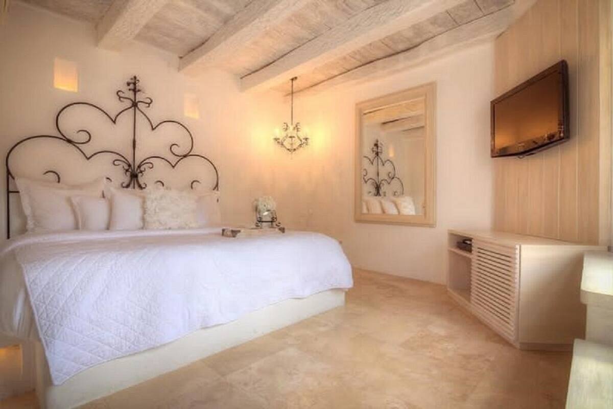 A bedroom with a bed, a bedside table, a mirror, and a wall-mounted TV.