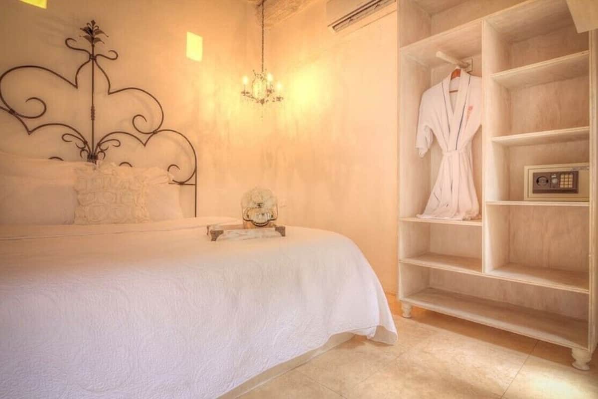 A bedroom with a bed, a chandelier, a white robe on a shelf, and a small decorative item on the bed.