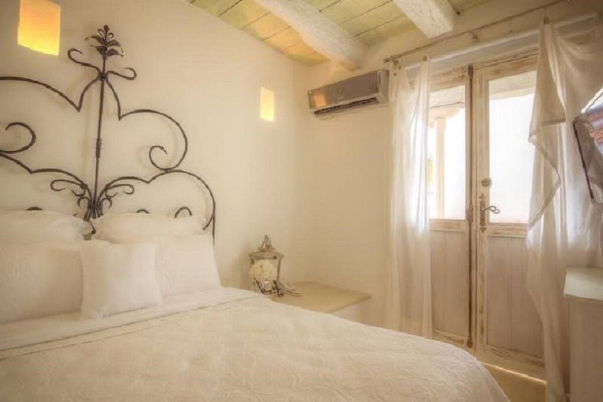A bedroom with a bed, a decorative wall piece, an air conditioning unit, and a window with curtains.