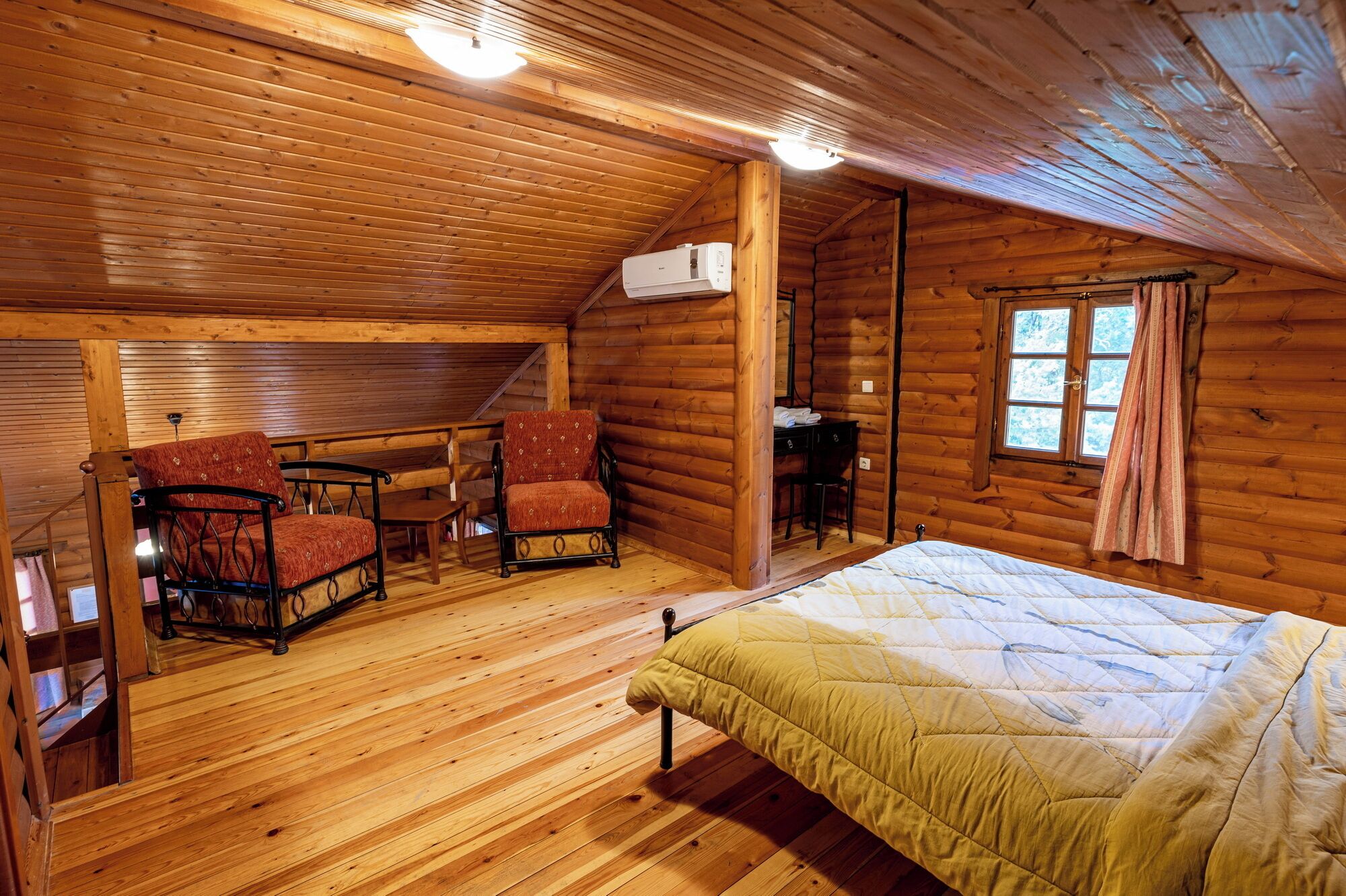 A log cabin bedroom with a bed, two chairs, a desk, and a window.