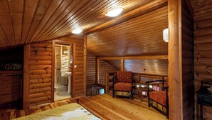 Een slaapkamer in een blokhut met een bed, een stoel, een klein tafeltje en een raam.