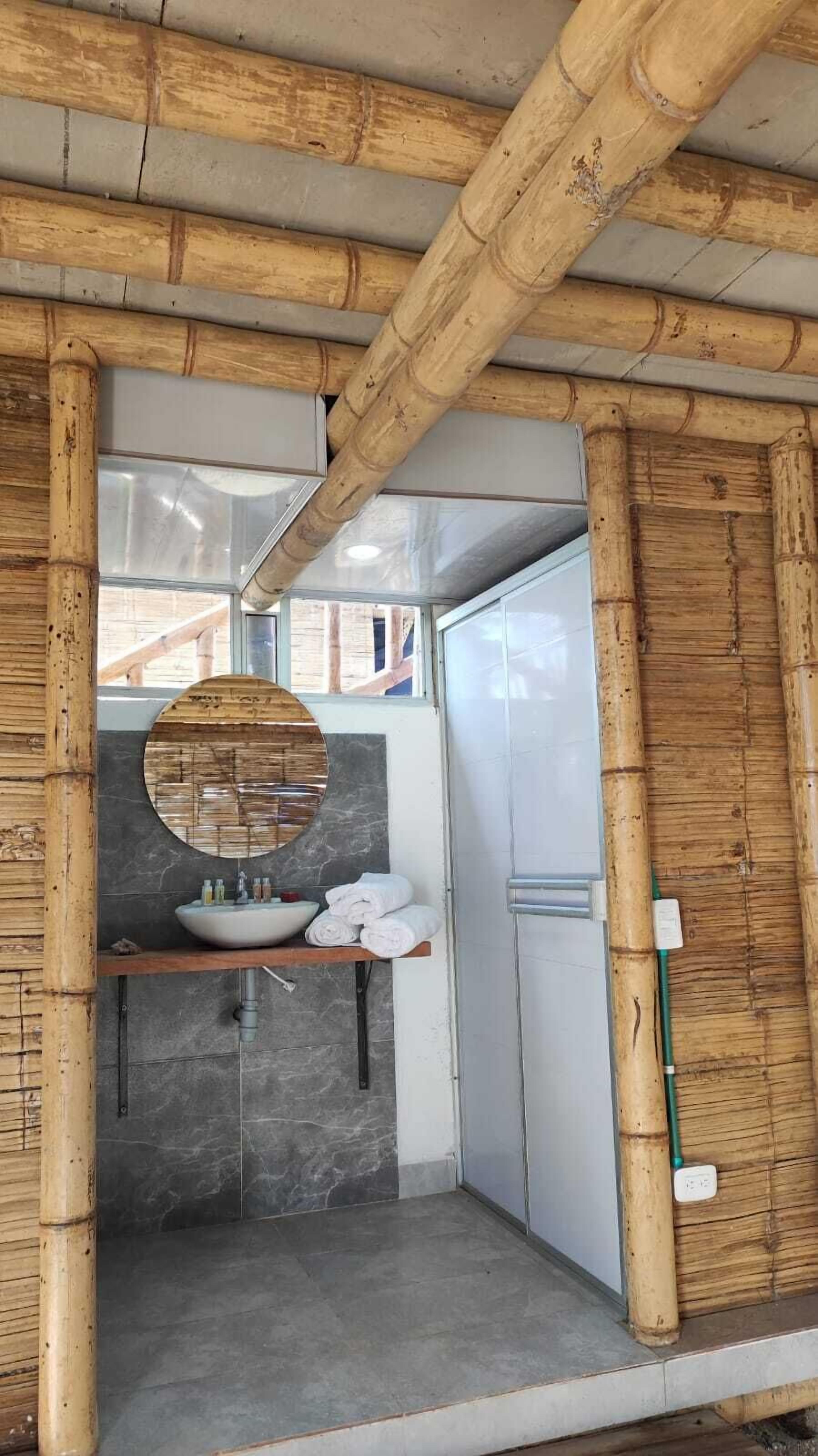 Une salle de bain avec un plafond en bambou, un miroir rond, un lavabo avec des articles de toilette et un porte-serviettes.