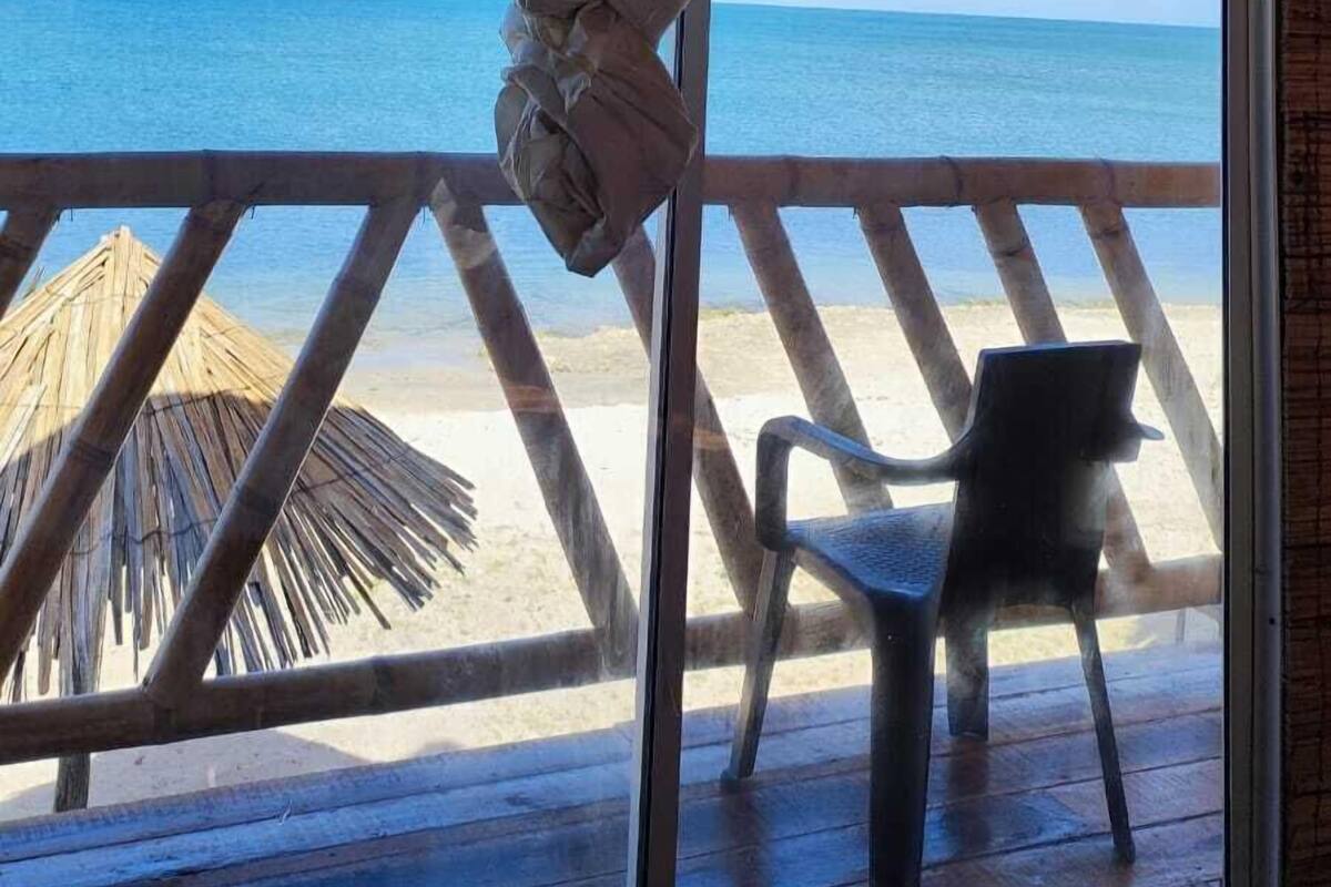 Un balcón de madera con vista al océano, una cortina colgante y una silla de plástico.
