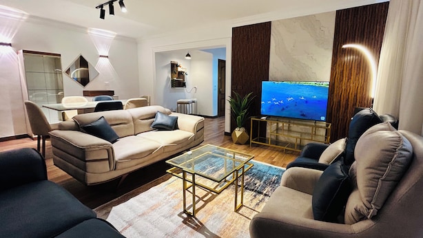 A modern living room with a beige sofa, a glass coffee table, and a flat-screen TV on a wooden stand.