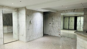 A spacious room with marble walls and a polished floor, featuring a large mirror and a modern light fixture.