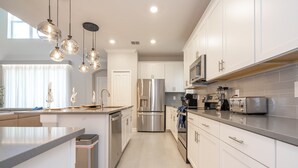 A modern kitchen with stainless steel appliances, white cabinetry, and pendant lighting. - DavenportMagicEscape 8964 (Davenport)