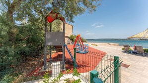 A playground with swings and a climbing structure, a beach with lounge chairs, and a clear view of the sea. - Stunning apartment in Ugrinic with WiFi (Ugrinic)