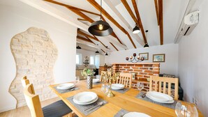 Un comedor con una mesa de madera dispuesta para cuatro, pared de ladrillo y vigas de madera a la vista en el techo.