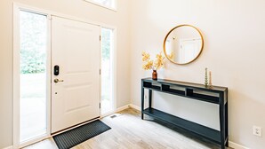 A modern entryway with a white door, a console table with a mirror, and a small vase with flowers.