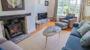 A cozy living room with a fireplace, a television, a sofa, and a window with curtains. - Tithe Barn Cottage (Dorchester)