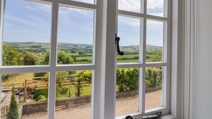 A room with a large window offering a view of a rural landscape, including fields and a distant hill. - Tithe Barn Cottage (Dorchester)