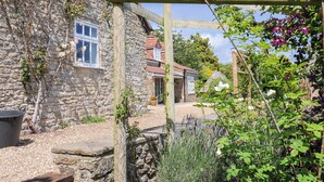A stone building with a window, a wooden trellis, and various plants. - Tithe Barn Cottage (Dorchester)