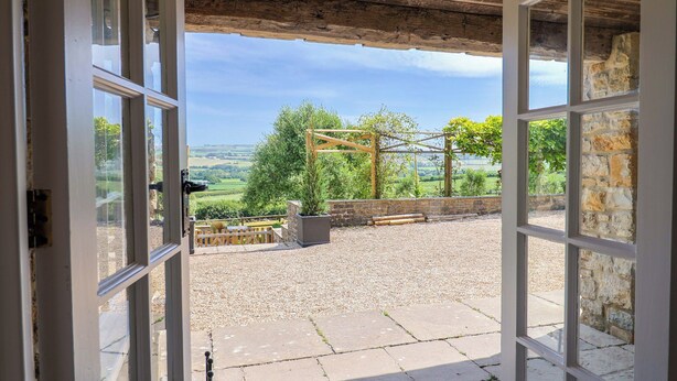 An open doorway leading to a gravel patio with a wooden pergola and potted plants. - Tithe Barn Cottage (Dorchester)