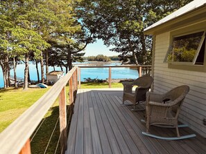Une terrasse en bois avec des fauteuils à bascule en osier donnant sur un lac.
