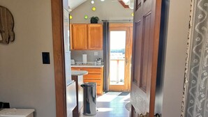 Een slaapkamer met een bed, een houten deur naar een keuken en uitzicht op buiten.