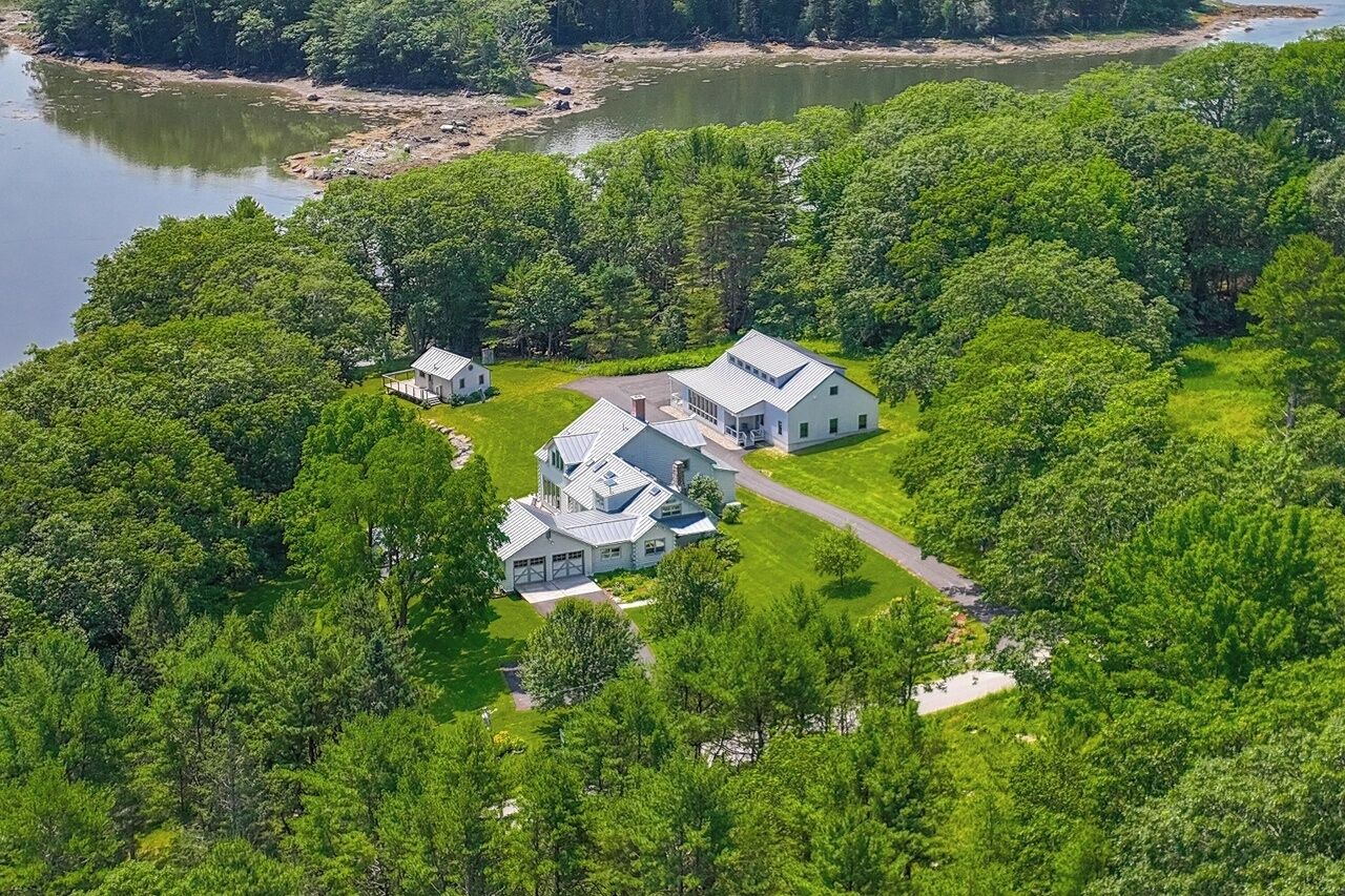 A large estate with multiple buildings surrounded by dense forest and a lake.