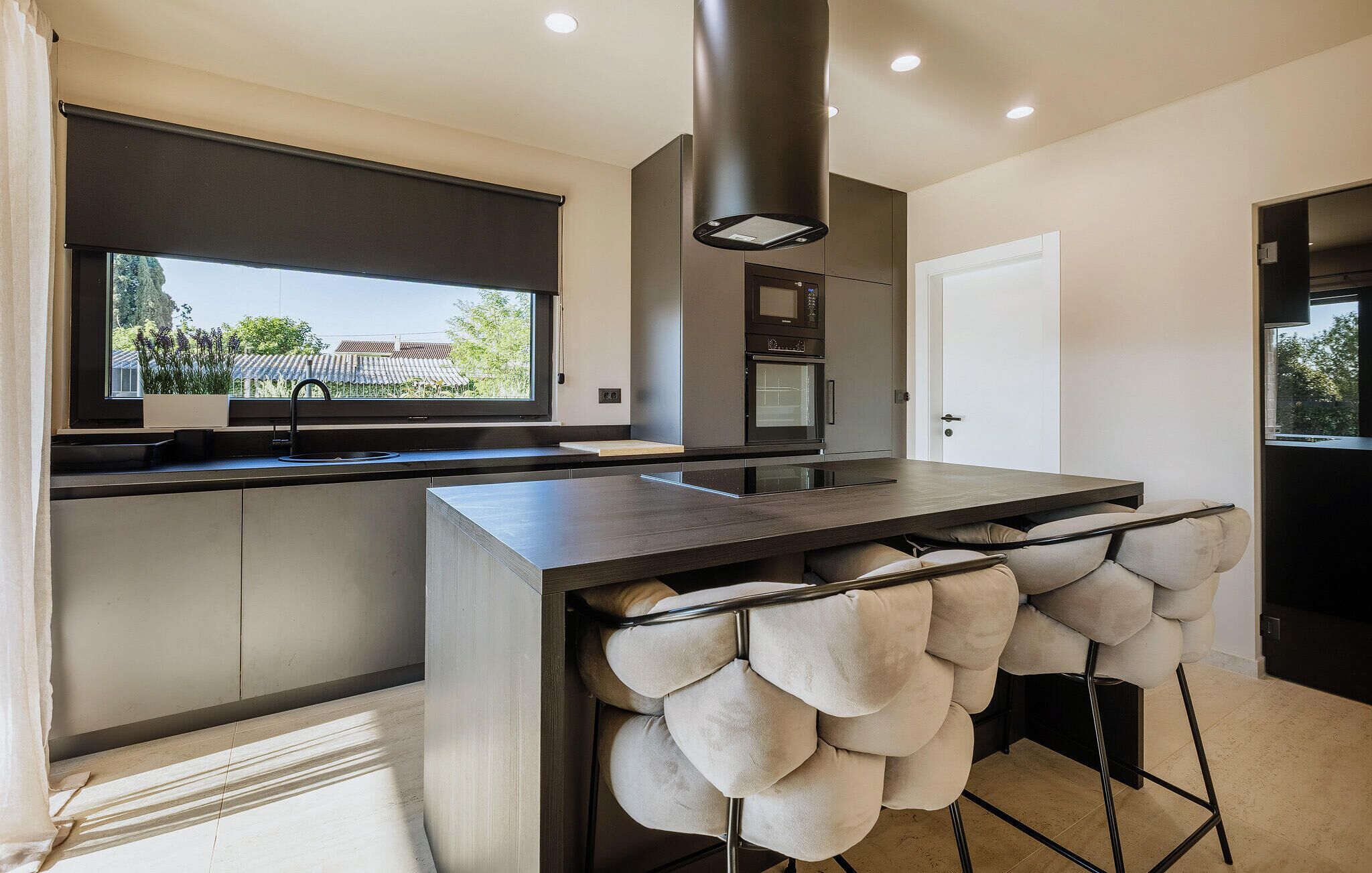Una cocina moderna con horno integrado, ventana con vistas y un espacio de asiento original con taburetes acolchados.