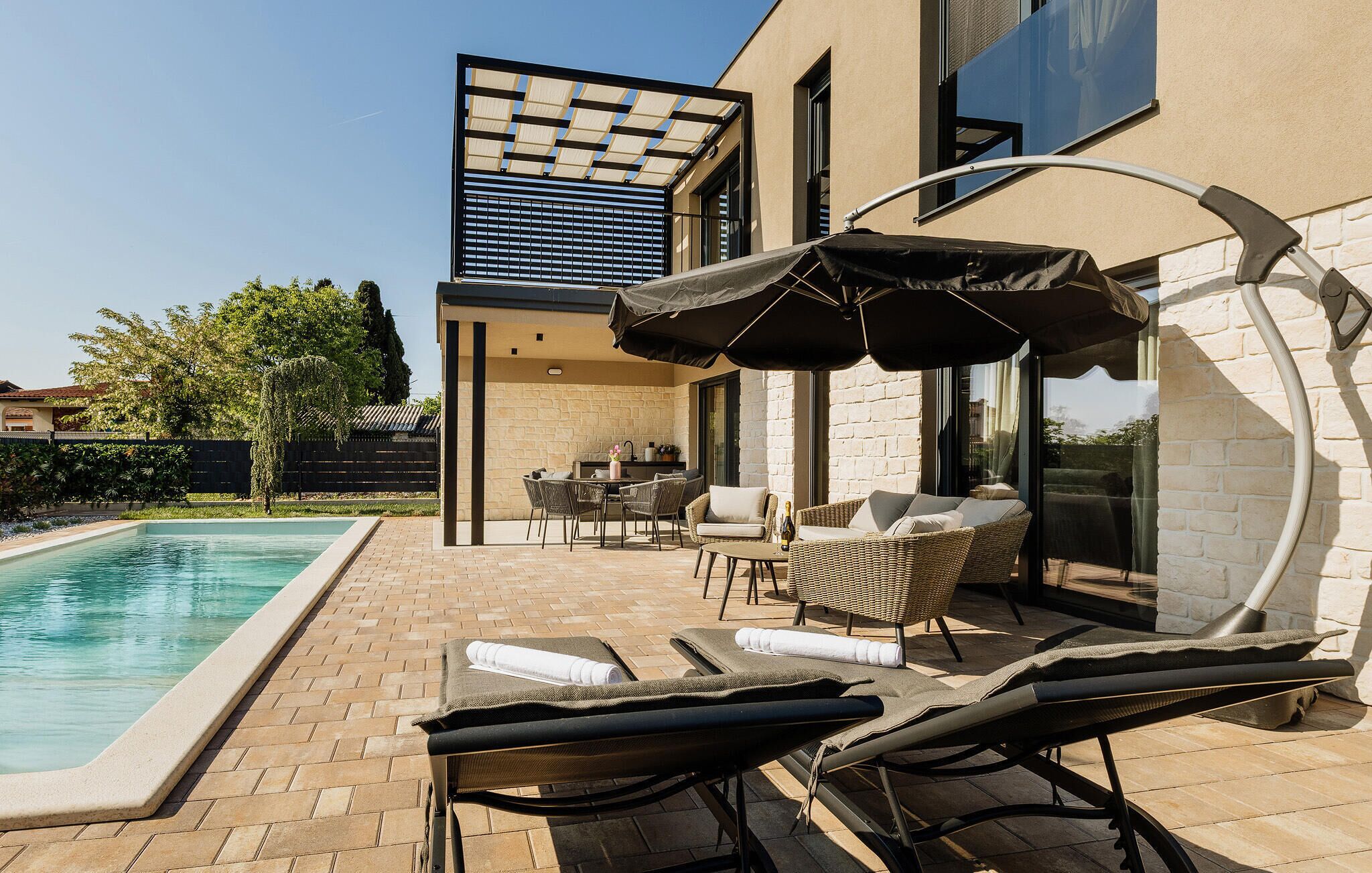 Un área de piscina moderna al aire libre con sillones de descanso y una zona de estar cubierta.