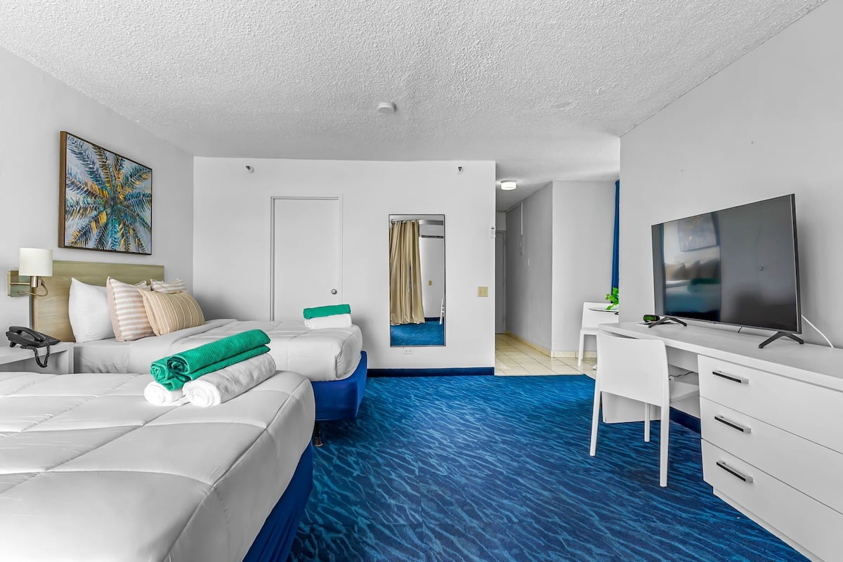 Ein Hotelzimmer mit Bett, Schreibtisch, Fernseher und einem durchgegangenen Tür sichtbaren Badezimmer.