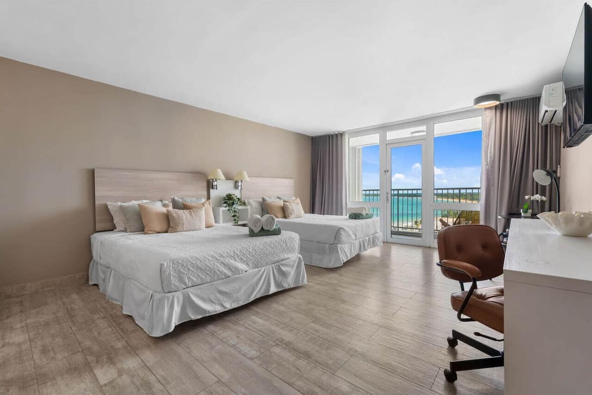 Ein Hotelzimmer mit zwei Betten, einem Schreibtisch und Blick auf den Ozean.