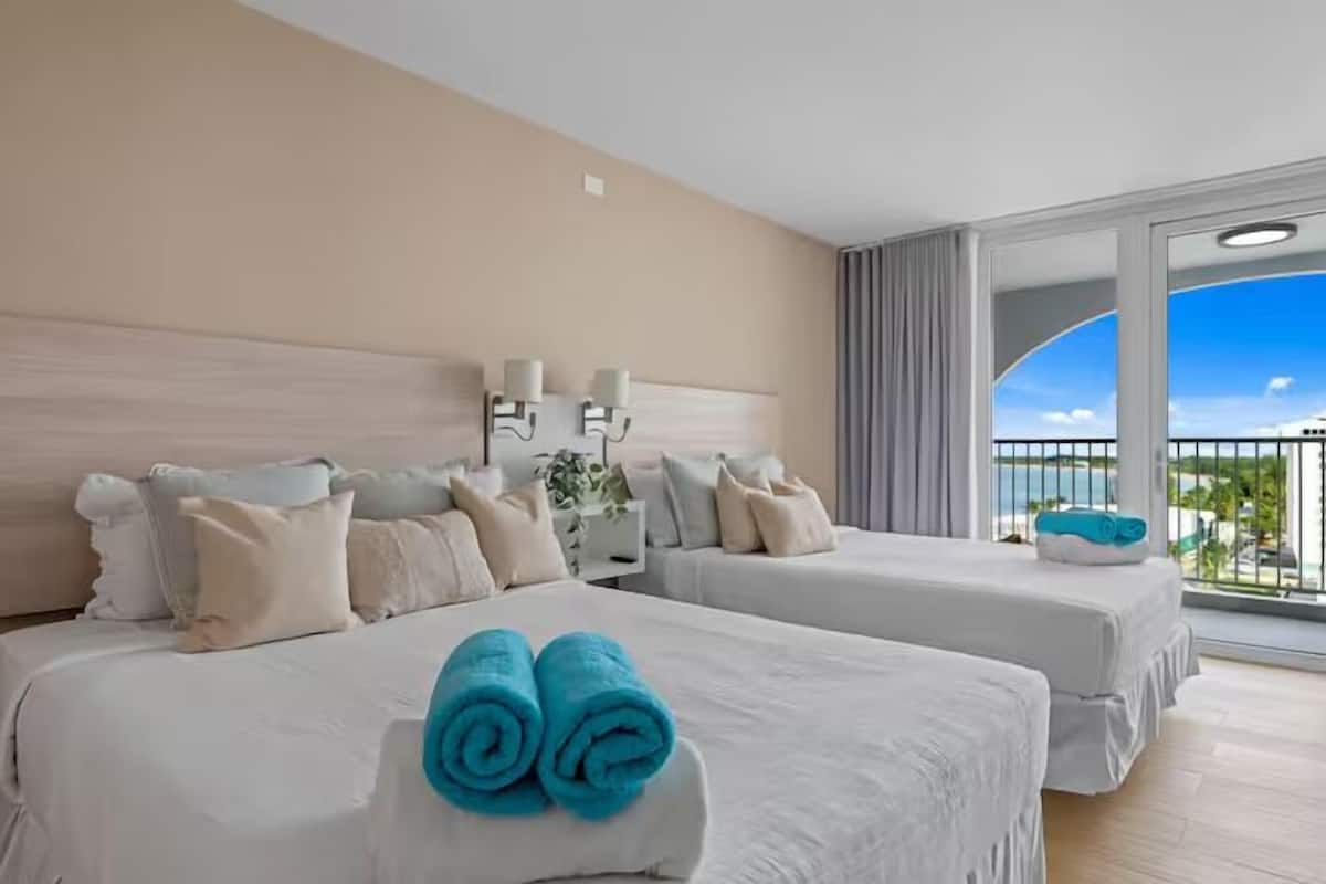 Ein Hotelzimmer mit zwei Betten, einem großen Fenster mit Meerblick und einem Balkon mit Geländer.