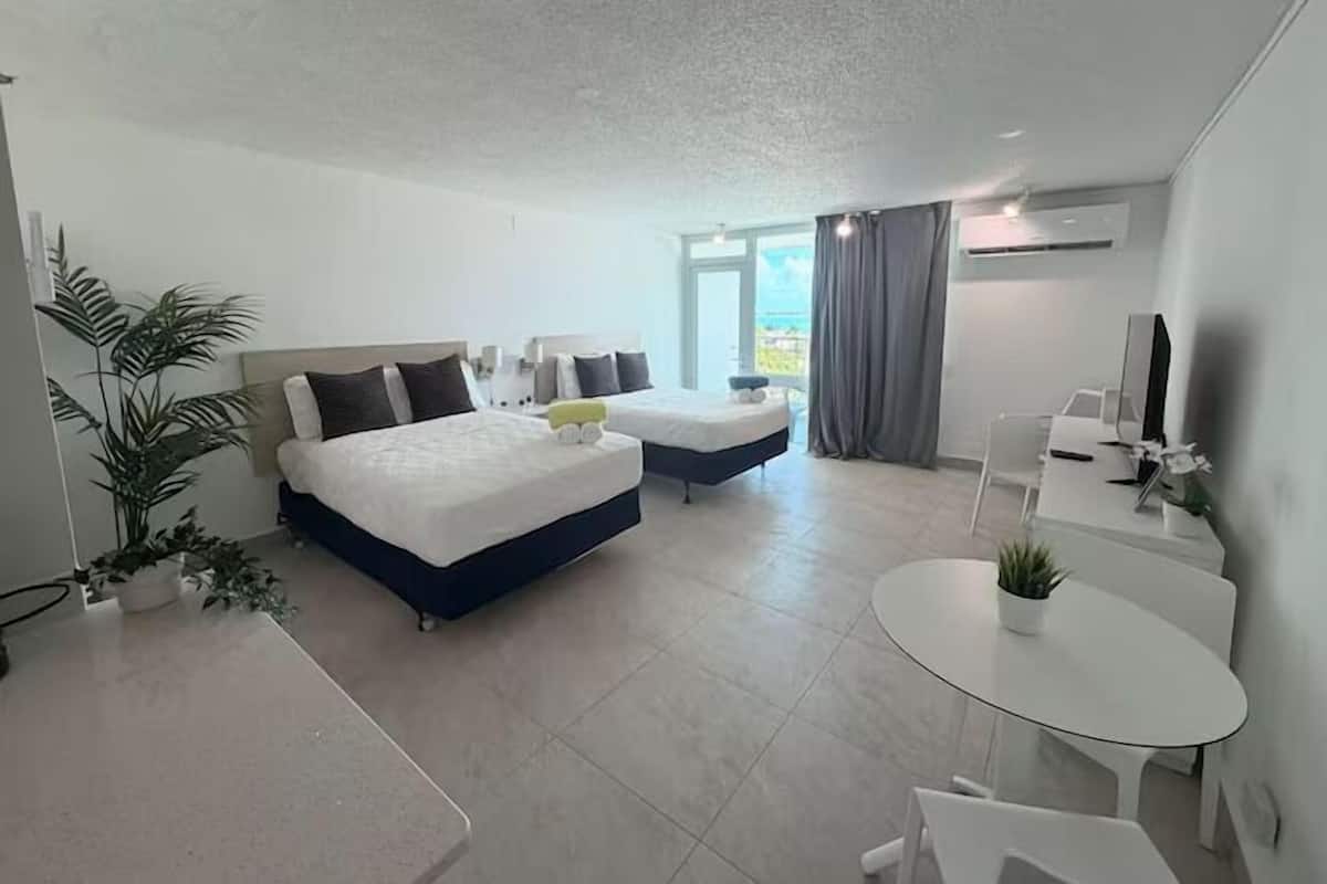 Ein modernes Hotelzimmer mit zwei Betten, einem kleinen Tisch, einem Fernseher und einem Balkon mit Blick.