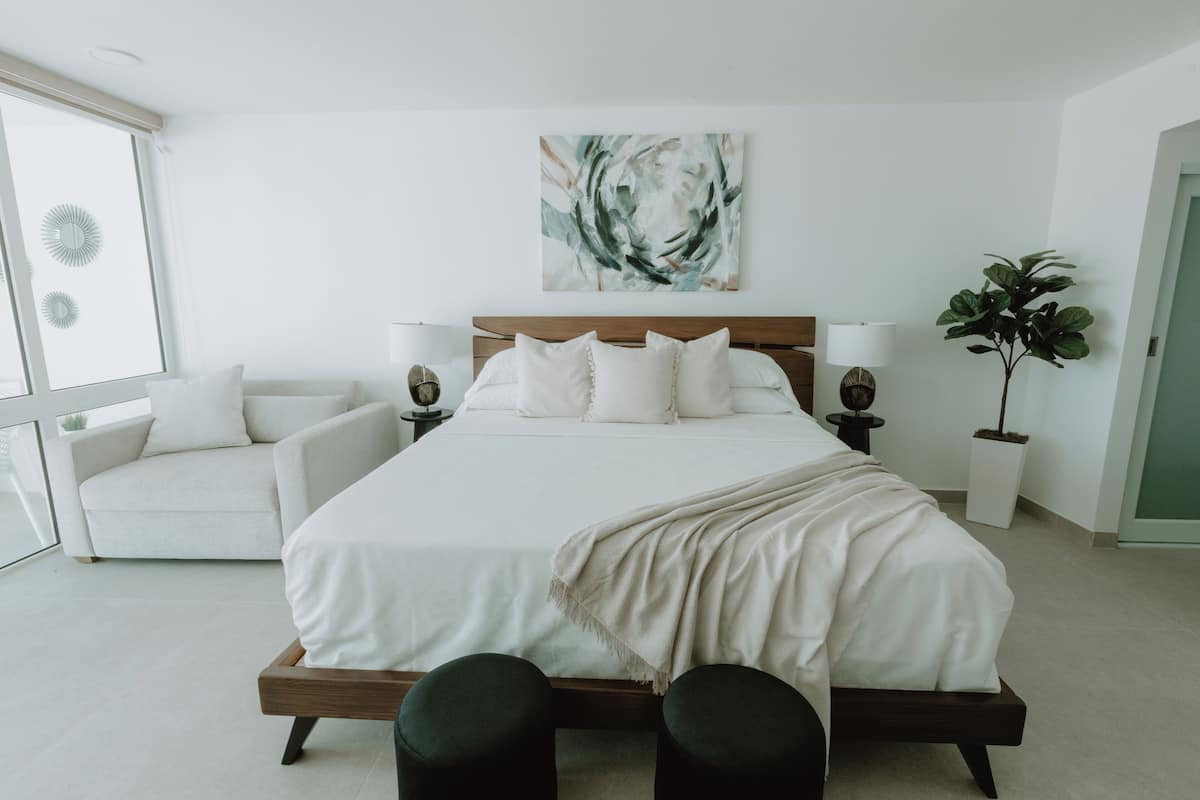 Ein modernes Schlafzimmer mit einem großen Bett, Nachttischlampen, einer Couch und einem Blumentopf.