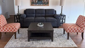 Een woonkamer met een donkere bank, twee fauteuils, een salontafel en een plafondventilator.