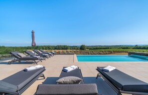 Ein Poolbereich mit Liegestühlen und Schwimmbecken mit Blick auf einen Weinberg und die entfernten Hügel.