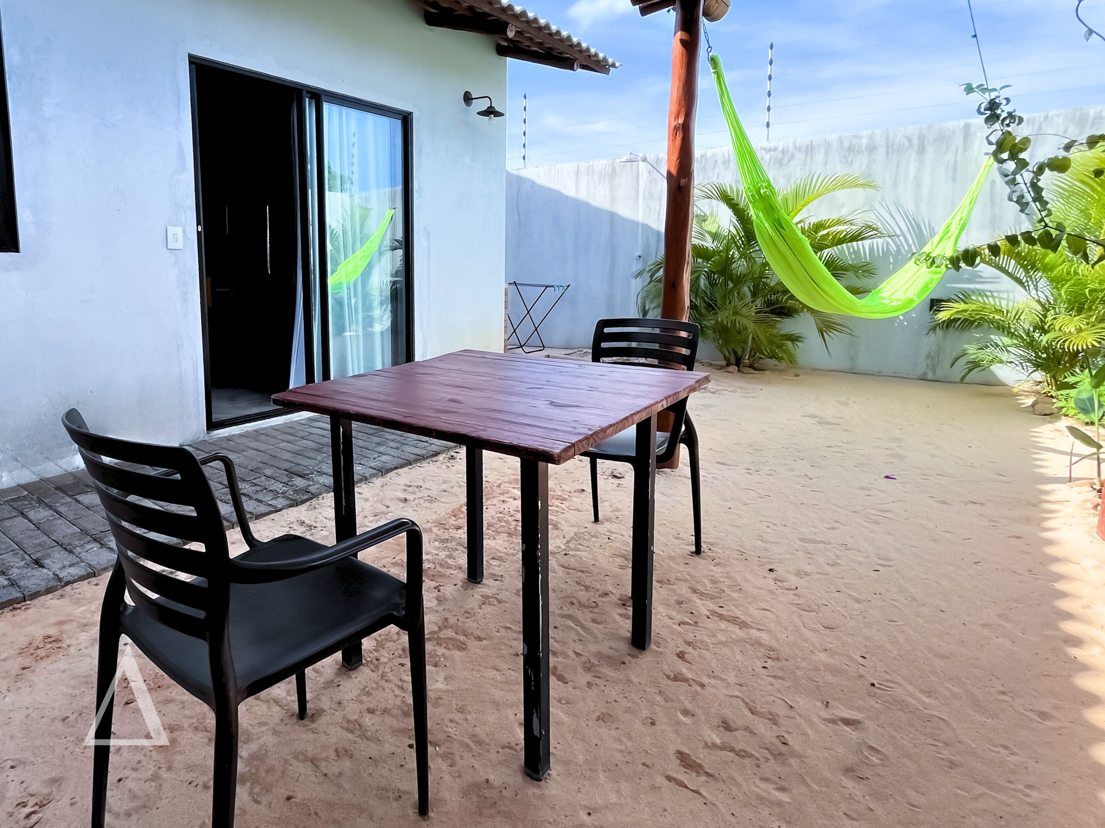 A patio with a wooden table and four chairs, a hammock, and a white building with a door and window.