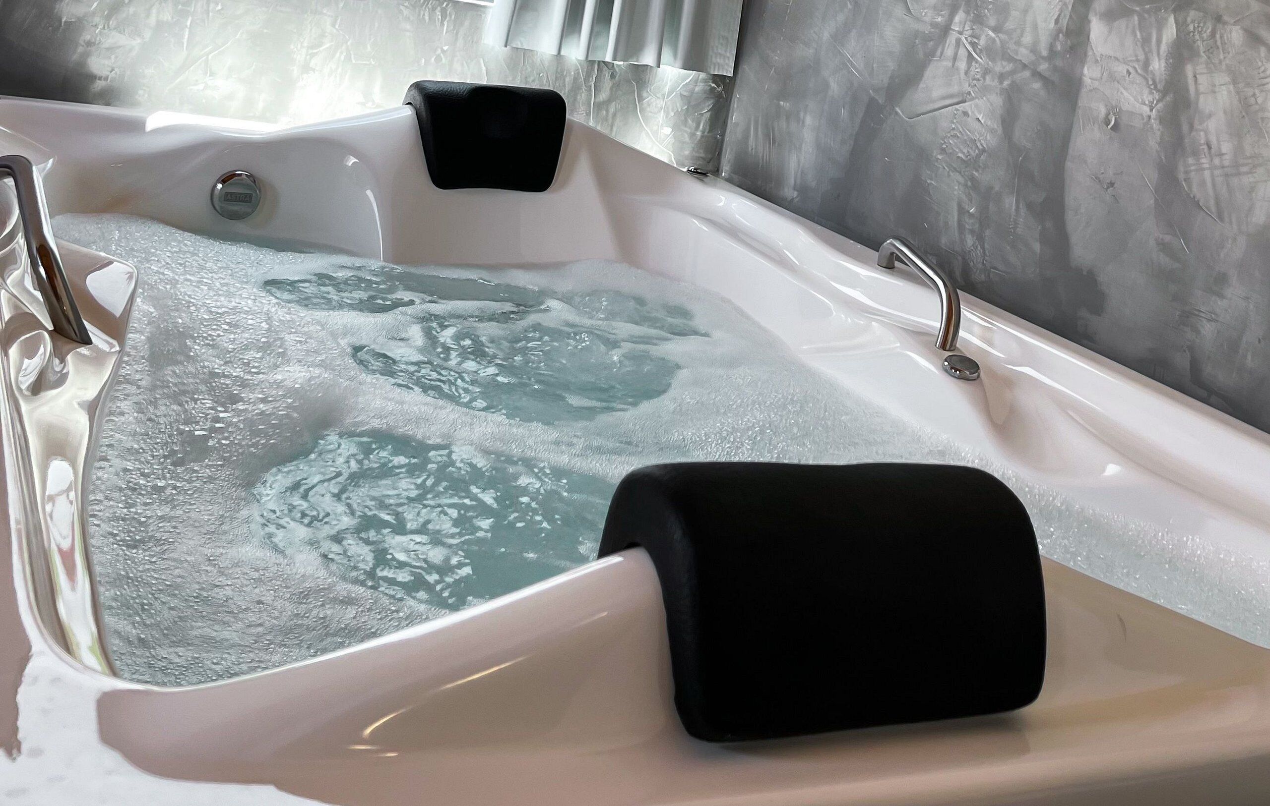 A hot tub with a black seat, a control panel, and a metallic faucet.