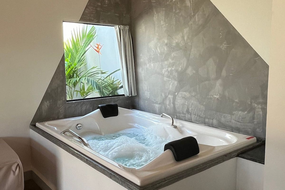 A modern bathroom with a freestanding bathtub, a large mirror, and a view of tropical plants.