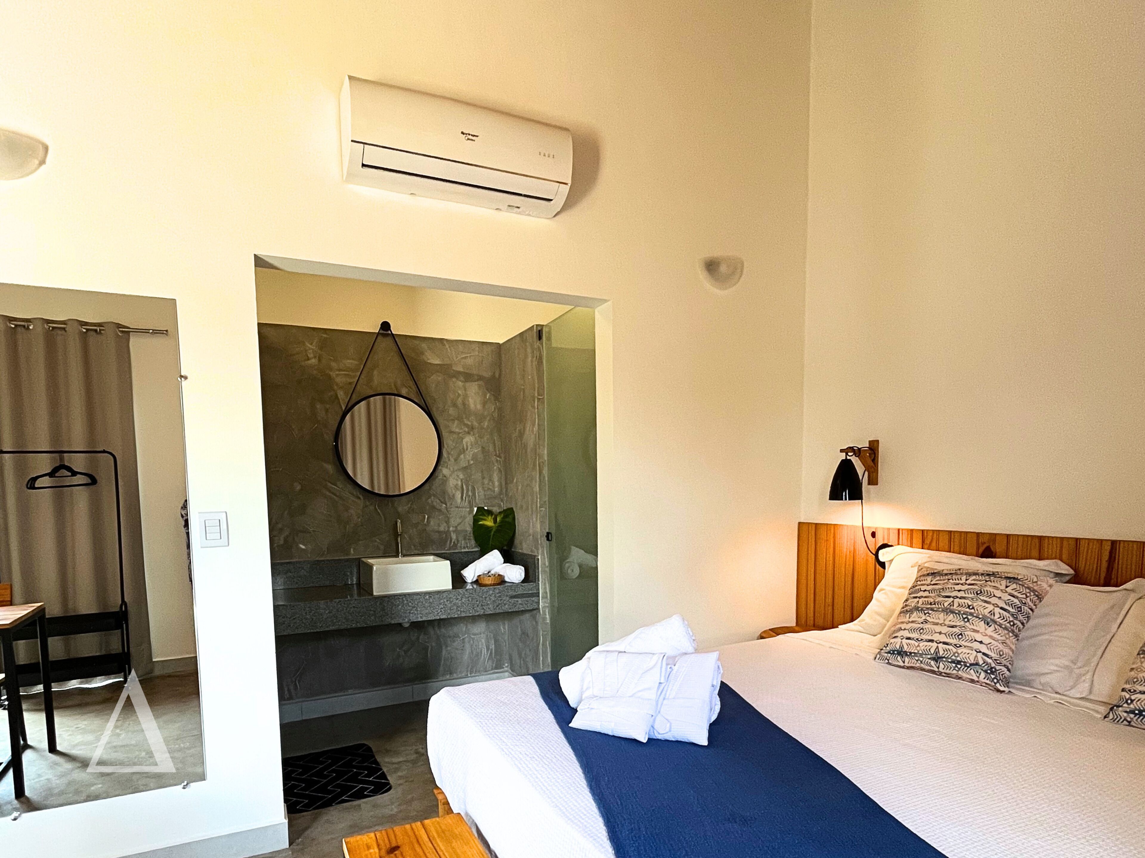 Hotelkamer met een bed, nachtkastje, lamp en een badkamer met een wastafel en spiegel.