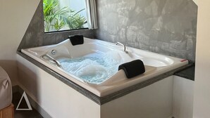 Un baño moderno con una bañera independiente, una ventana con vistas a zonas verdes y una pared con textura de piedra.
