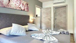 A hotel room with a bed, pillows, a robe, towels, a painting, a wardrobe, and an air conditioning unit. - Awesome home in Baska (Baska)