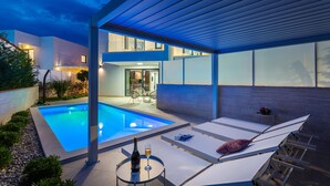 A modern outdoor pool area with lounge chairs and a table with a bottle of champagne.
