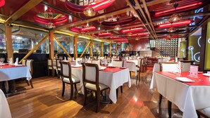 A restaurant with multiple tables and chairs, wooden floors, and a modern ceiling design with red lighting.