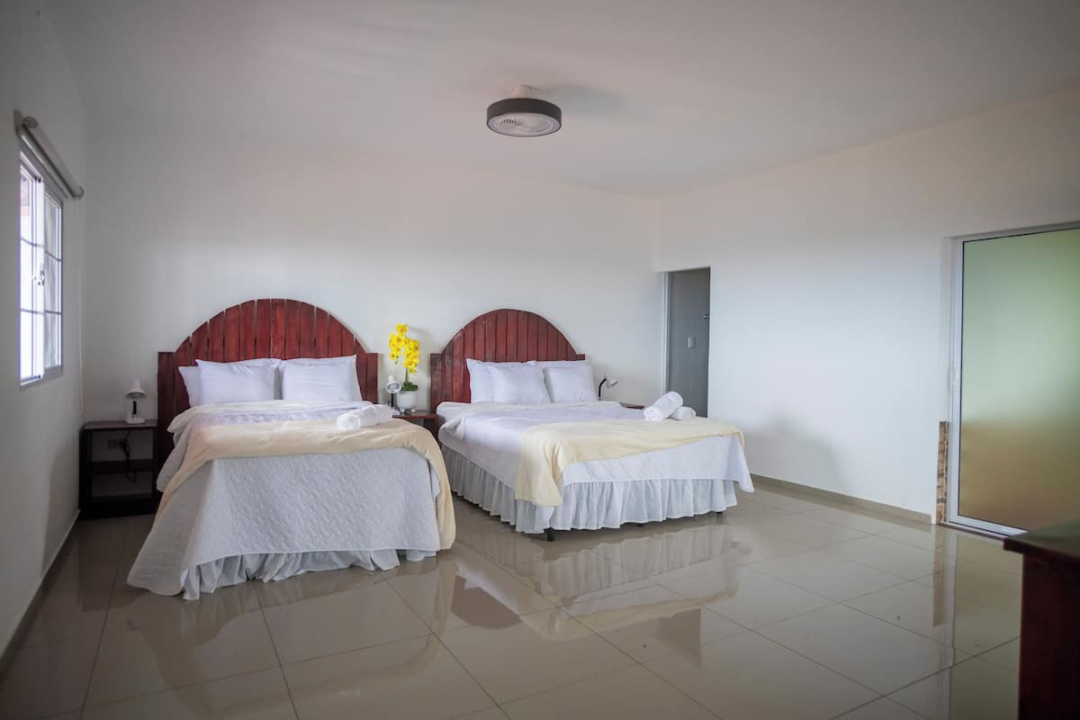 A hotel room with two beds, a nightstand, a lamp, and a window.