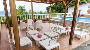 A covered outdoor seating area with white furniture and a pool in the background. - Summit 503 Rental Villas (Santa Tecla)