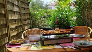 An outdoor dining area with a table set for two, featuring a grill, plates, cutlery, and a bottle. - Vacation apartment with swimming pool & 400m from the beach (Vallauris)