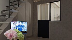 A modern interior with a staircase, a television displaying a program, and a decorative flower arrangement. - Vacation apartment with swimming pool & 400m from the beach (Vallauris)