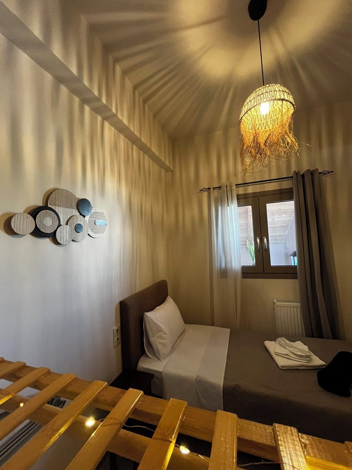 Une chambre à coucher avec un lit, un luminaire suspendu, une fenêtre avec des rideaux et des éléments de décoration murale.