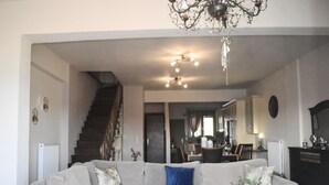 Una sala de estar moderna con un sofá seccional gris, una mesa de centro y una araña. Se ve una escalera al fondo que conduce a otro nivel.