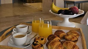 A breakfast tray with croissants, juice, and coffee in a room with stone arches and a tiled floor.