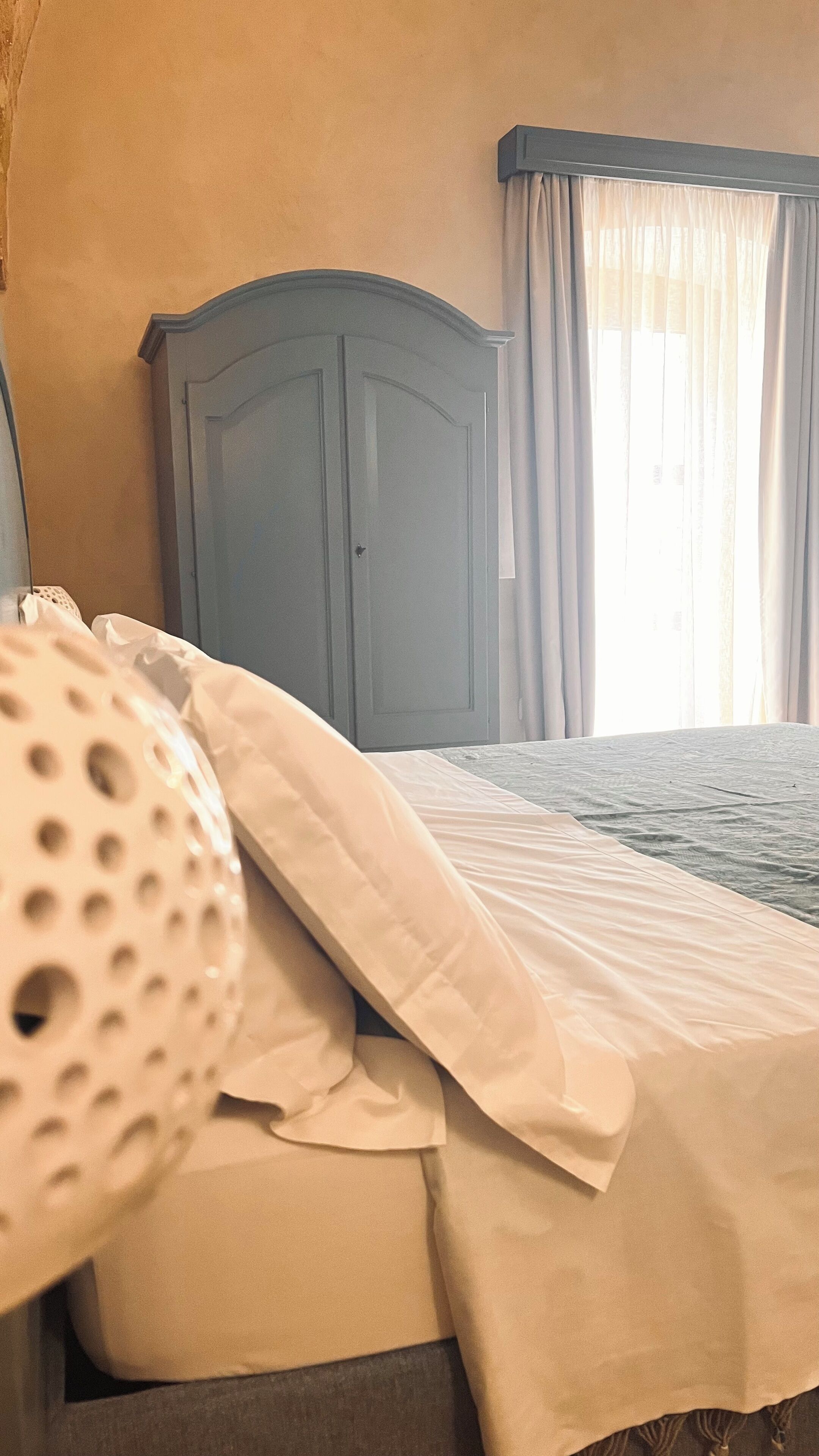 A bedroom with a bed, a wardrobe, and a window with curtains.