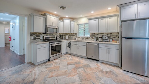 A modern kitchen with white cabinets, stainless steel appliances, and a patterned tile floor. - 3 bed 2 bath house with 2 king beds, fire pit, gazebo & pool table! (Roswell)