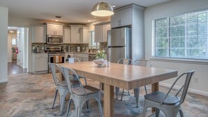A modern kitchen with white cabinets, stainless steel appliances, and a large dining table with chairs. - 3 bed 2 bath house with 2 king beds, fire pit, gazebo & pool table! (Roswell)