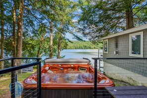A hot tub with a view of a lake and forest, surrounded by trees and a building with a window.