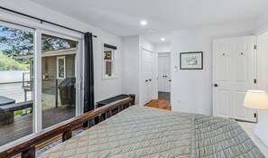 A bedroom with a large bed, a bench, a sliding glass door to a balcony, and a door leading to another room.